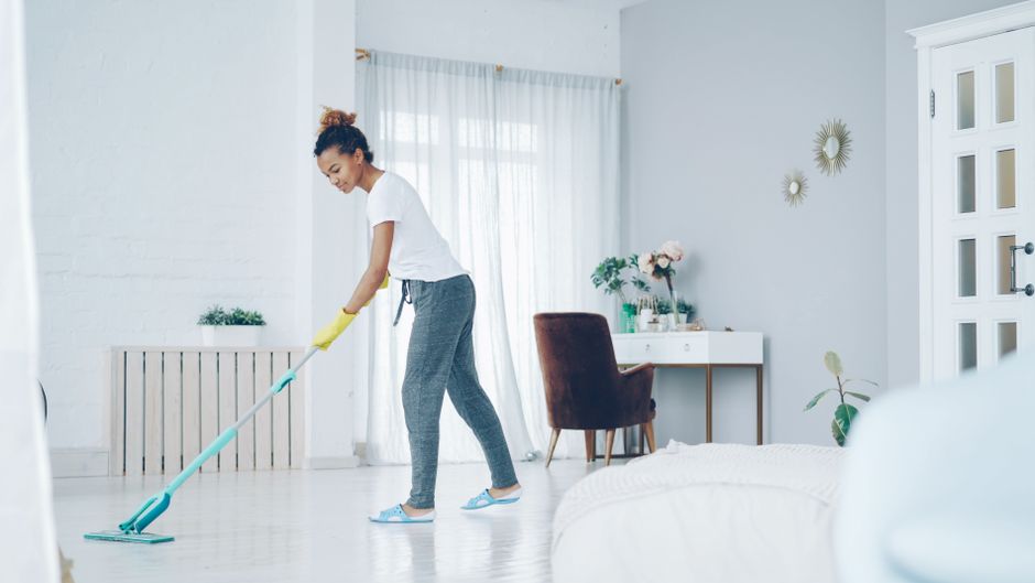 A woman cleaning a bright, modern living room with a mop, creating a clean, welcoming space.